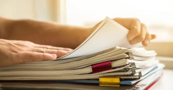 combien de temps garder les papiers d'assurance habitation Une personne feuillette une pile de dossiers attachés avec des trombones colorés, symbolisant la gestion et l'organisation des documents importants liés à l'assurance habitation