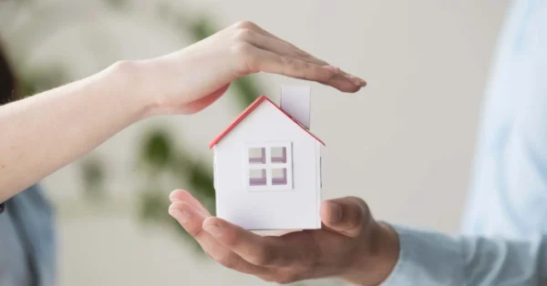 comment résilier son assurance habitation Une maison miniature protégée par des mains symbolisant la sécurité et la couverture d'une assurance emprunteur