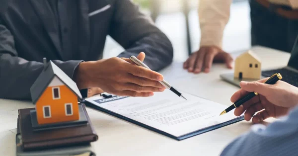 peut on avoir 2 assurances habitation un bureau où des personnes sont en train de signer un contrat, avec un modèle de maison posé sur des livres à proximité